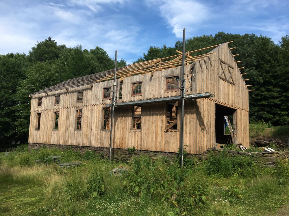 Inside a timber frame structure during construction, with heavy beams and scaffolding