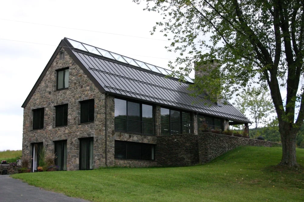 Custom stone home with a steep standing-seam metal roof and tall windows on a green lawn